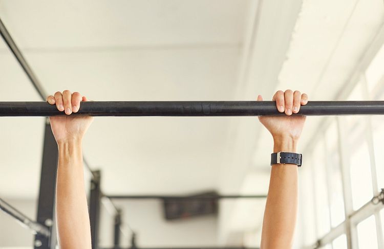 Feminine white hands and wrists grip a black pullup bar as if hanging from it. 