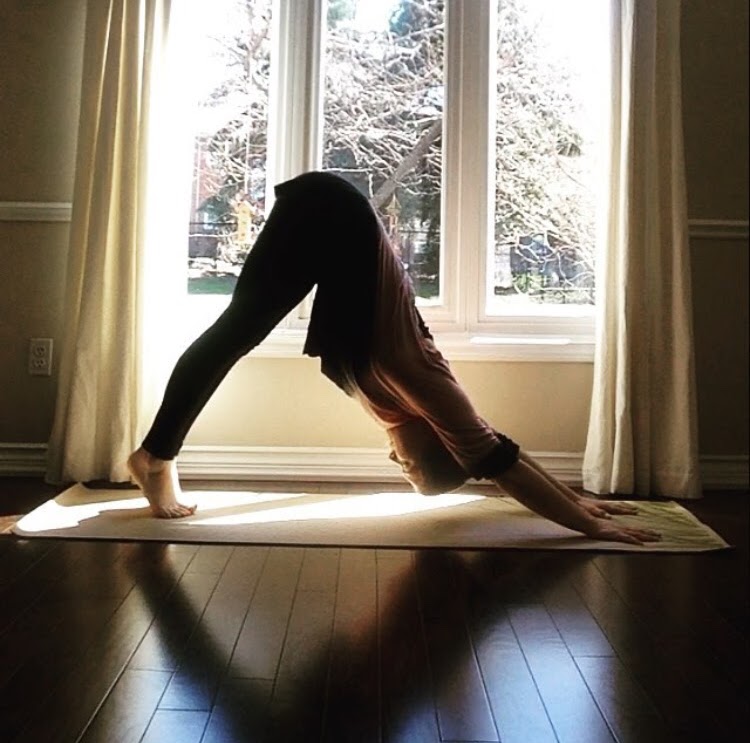 A young white woman does a downward dog position in a sunny room.